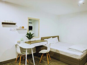 A bedroom with a wooden bed, white bedding, a desk with two white chairs, a mirror, and a small shelf with items. - Cozy 1-bedroom apartment in perfect Quảng Nam with AC (Quảng Nam)