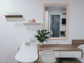 A modern hotel room with a white table, a wooden sideboard, a mirror, and a potted plant. - Cozy 1-bedroom apartment in perfect Quảng Nam with AC (Quảng Nam)