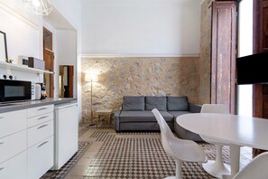 A compact living space with a kitchenette, a sofa, a dining table, and a patterned floor. - López Studio (Las Palmas de Gran Canaria)