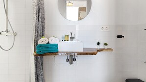 Een badkamer met een douche, wastafel, spiegel en handdoekhouder.