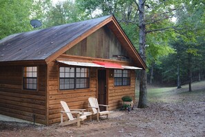 Tunnelmallinen hirsihökkelö, jonka edessä on kaksi Adirondack-tyylistä puutarhatuolia, katolla satelliittiantenni ja ovessa kyltti, jossa lukee: ”Shady Brook Resort”.