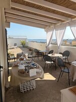 Un patio al aire libre con mesas y sillas, un espacio tipo bufé y vista al mar.