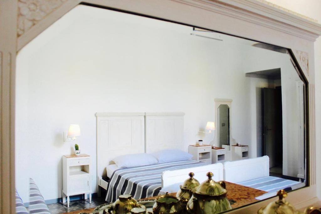 Un dormitorio con cama, mesitas de noche, un espejo y objetos decorativos.