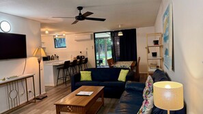 A living room with a sofa, coffee table, and a TV. There's a kitchen area with a dining table and chairs. - Baden 2 - Rainbow Shores (Rainbow Beach)