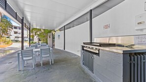 An outdoor seating area with white plastic chairs and a grill station. - Baden 2 - Rainbow Shores (Rainbow Beach)