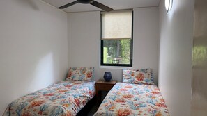 A small room with two single beds, a ceiling fan, a window with a view of greenery, and a small table with a vase. - Baden 2 - Rainbow Shores (Rainbow Beach)