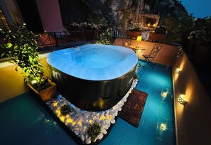 A hot tub surrounded by a stone border, a small table with a lamp, and potted plants. - La Maison Rose - Gaetano Capone (Maiori)