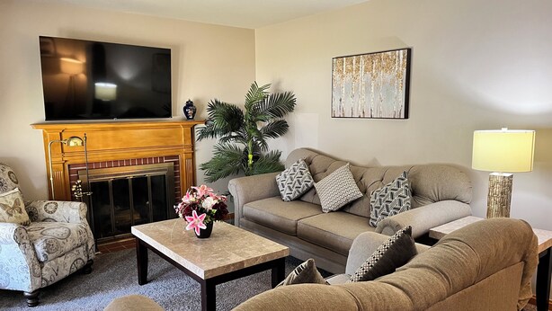 A living room with a fireplace, sofa, armchair, coffee table, and a TV mounted on the wall. - Spacious 3 level 4-bedroom house- 2 Full kitchens-2 king beds and 3 queen beds. (Campbell)
