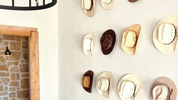 Una habitación con pared de piedra, un banco de madera y una exhibición de varios sombreros fijada a la pared.