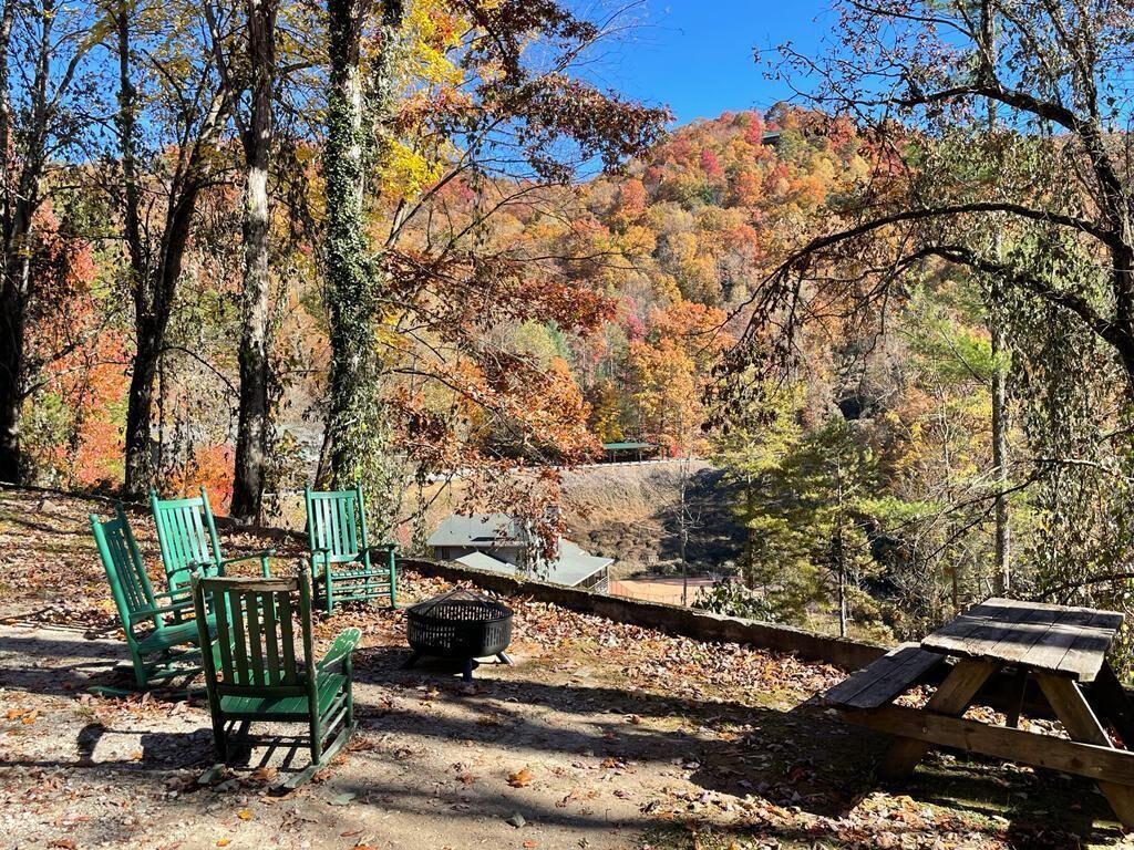 Un camping con sillas verdes, una mesa de picnic y una fogata.