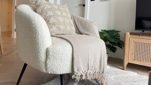 Ein modernes Wohnzimmer mit einem weißen Sessel, einer beige farbenen Decke und einem Holztisch mit einem Fernseher.