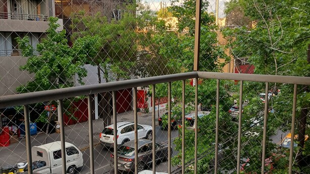 A balcony with a view of a busy street, parked cars, and buildings in the background. - Apartment steps from the subway and tourist sites (Santiago)