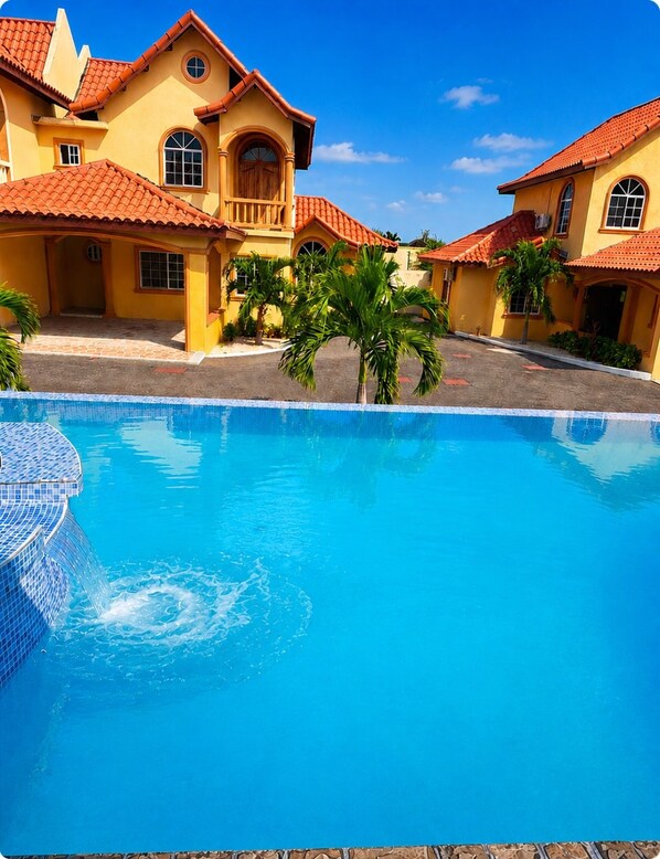 A swimming pool with a tiled edge, surrounded by buildings with red-tiled roofs and yellow walls.