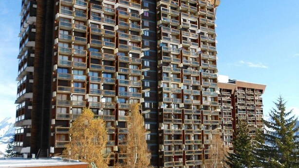 A high-rise hotel with multiple balconies, a ski slope in the background, and a snowy landscape. - 100m from ski slopes, 18th floor, view mountain, swimming pool, balcony, tv, ski locker, 22m² (Le Corbier)