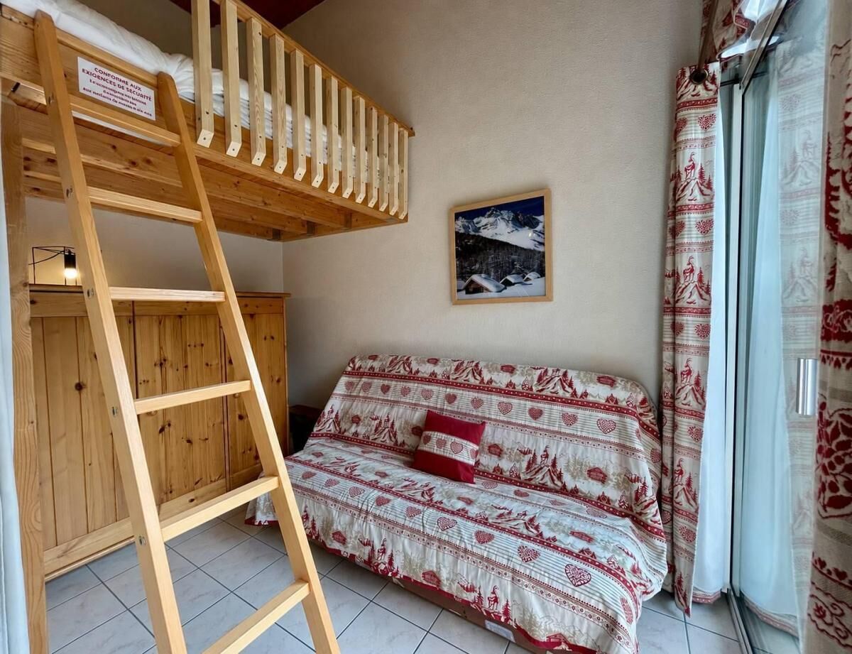 A bunk bed with a ladder, a sofa with patterned upholstery, a framed picture on the wall, and a window with curtains.