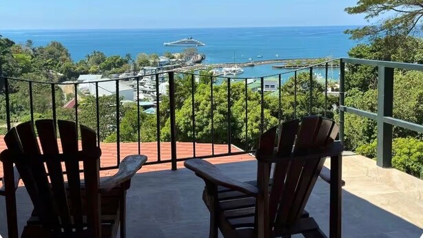Varanda com duas cadeiras de madeira de frente para uma marina e o oceano.