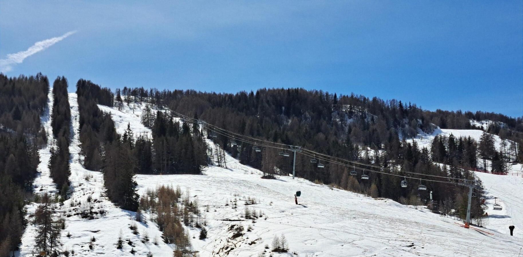 A ski slope with a chairlift, trees, and a clear sky.