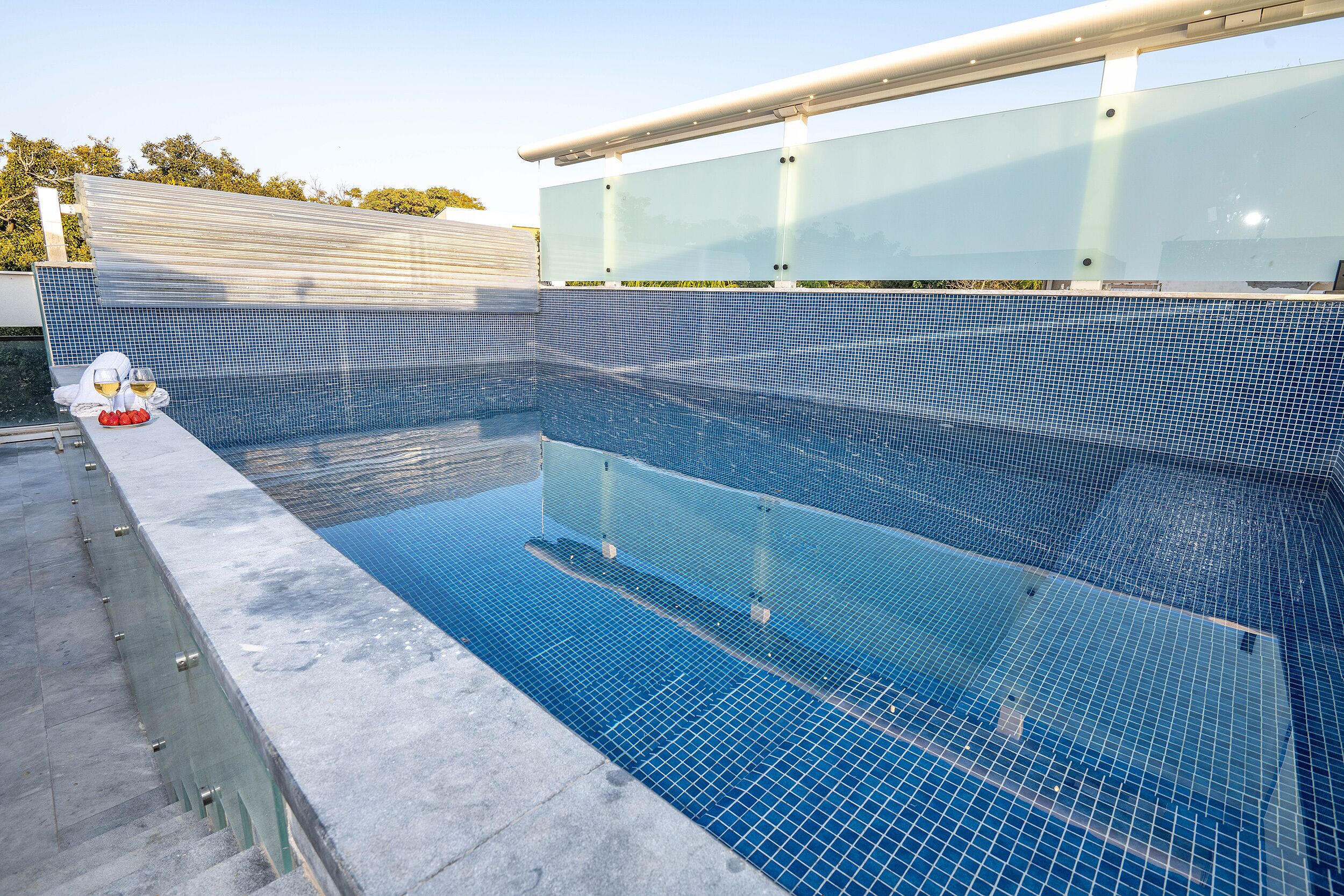 A swimming pool with clear blue water, surrounded by a tiled deck and a glass barrier.