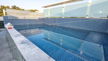 A swimming pool with clear blue water, surrounded by a tiled deck and a glass barrier.