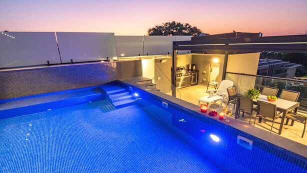 Ein Pool auf dem Dach mit Küchen- und Essbereich, umgeben von einem Glasgeländer.