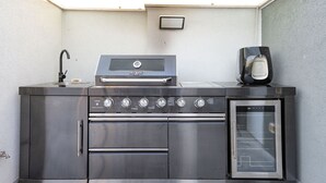 Eine Outdoor-Küche aus Edelstahl mit integriertem Backofen, einer Kaffeemaschine und einem Spülbecken.