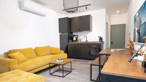 Ein modernes Wohnzimmer mit einem gelben Sofa, einem Holztisch und einer Küchenzeile mit dunklen Schränken und einer Holz Arbeitsplatte.