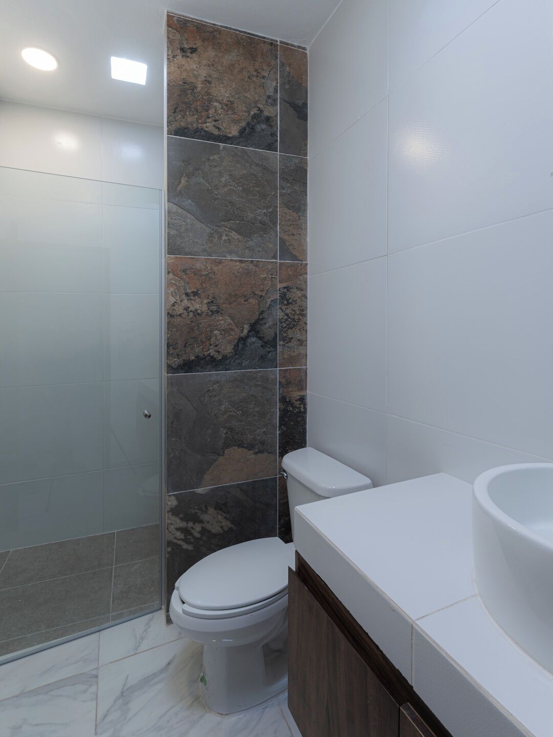 A bathroom with a glass shower enclosure, a toilet, and a sink with a wooden vanity.