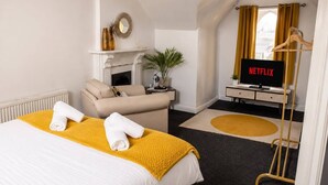 Une chambre d’hôtel avec un lit, un canapé, une télévision et une cheminée.