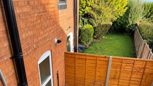 Une petite terrasse avec du gazon synthétique, deux chaises en osier et une clôture en bois.