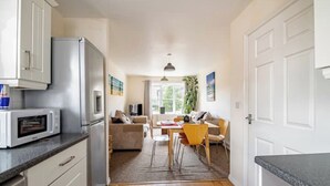 Una cocina moderna con microondas y refrigerador integrados, un comedor con mesa y sillas de madera, y una sala de estar con sofá y televisor.