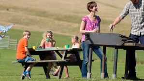 Un montaje para picnic en un campo cubierto de hierba, con una mesa de picnic y gente sentada alrededor.