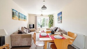 Una sala de estar acogedora con un sofá, una mesa de comedor para dos personas y un televisor sobre un mueble bajo.