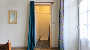 A bathroom with a shower, a wooden floor, a mirror, and a door with a curtain. - Le Clos Vendéen - Piscine Privée (L'Hermenault)
