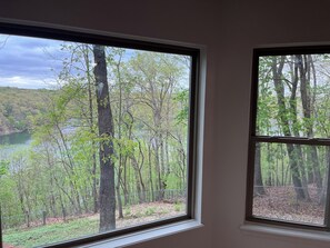Ein Zimmer mit zwei Fenstern, Blick auf eine bewaldete Landschaft mit einem See.