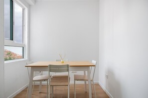 Ein kleiner Raum mit weißen Wänden, einem Holztisch und vier weißen Stühlen.