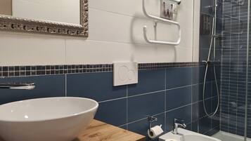 Un baño con un lavamanos blanco, un espejo con marco decorativo, un perchero y una zona de ducha con azulejos azul oscuro.