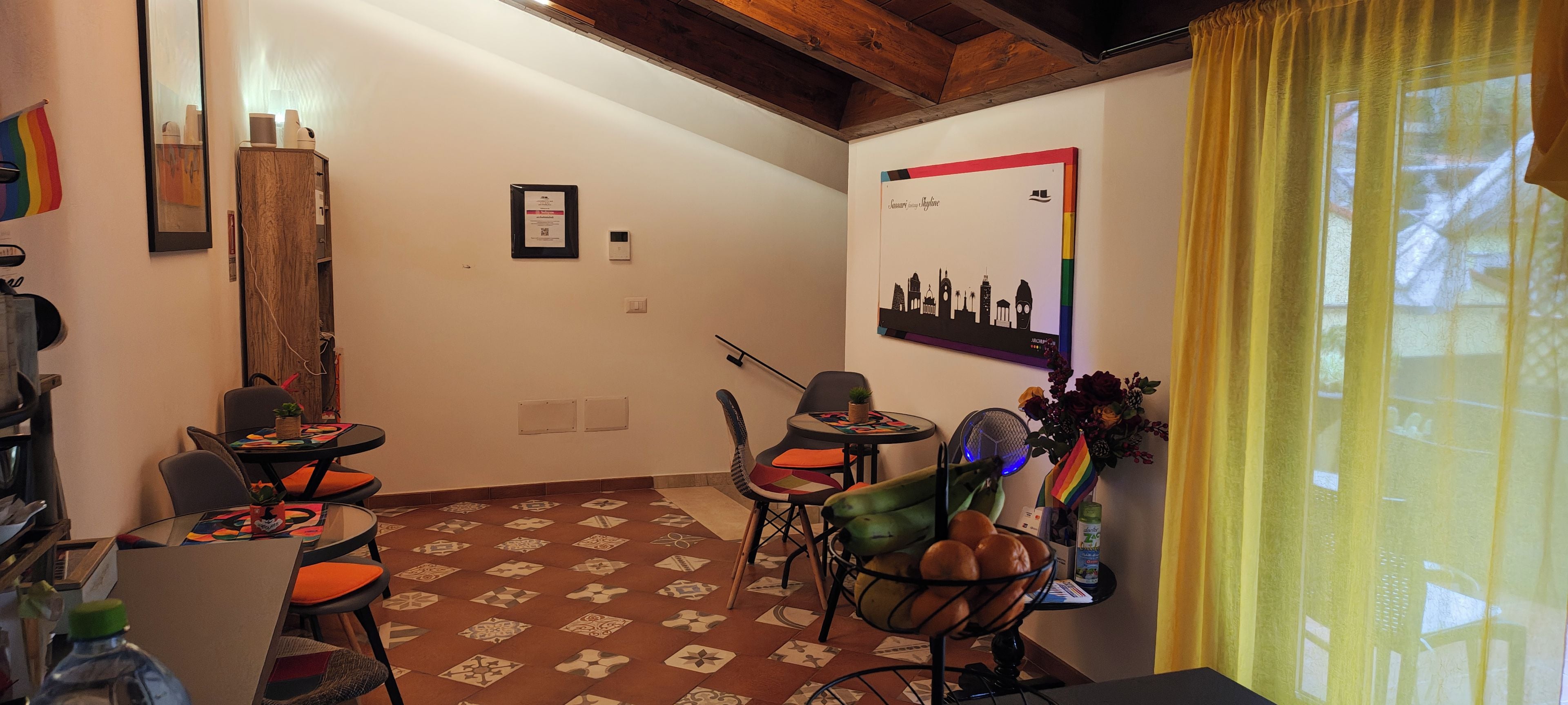 Ein gemütliches Zimmer mit einem gemusterten Boden, einem Essbereich mit Stühlen und einem Tisch, einem an der Wand befestigten Kunstwerk und einem Fenster mit gelben Vorhängen.