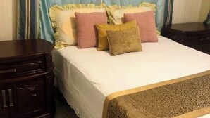 A neatly made bed with a white bedspread and decorative pillows, a wooden nightstand to the left, and a patterned rug at the foot of the bed. - CLASSIC 1970'S STYLE HOUSE NEXT TO THE BEACH (Rio San Juan)