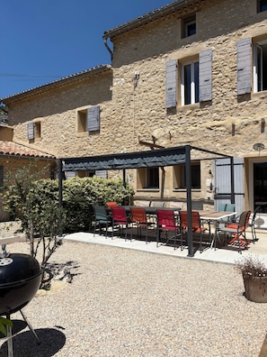 A stone building with a covered outdoor seating area, a barbecue grill, and a gravel patio. - Gite for 15p at the foot of Mont Ventoux_Lacets du Ventoux (Beaumont-du-Ventoux)