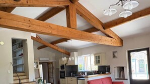 A spacious kitchen with wooden beams, a dining area with a large table and chairs, and a red sofa. - Gite for 15p at the foot of Mont Ventoux_Lacets du Ventoux (Beaumont-du-Ventoux)