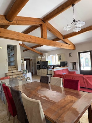 A spacious kitchen with wooden beams, a dining area with a large table and chairs, and a red sofa. - Gite for 15p at the foot of Mont Ventoux_Lacets du Ventoux (Beaumont-du-Ventoux)