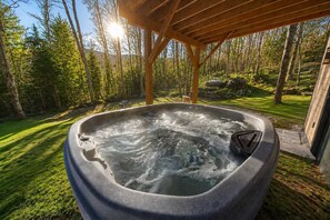 A hot tub in a forested area with a wooden pergola overhead. - Spa & Foosball | Le WKD (Saint-Philémon)