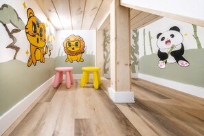 Une salle de jeux pour enfants avec un plancher en bois, deux tabourets et des peintures murales représentant un tigre, un lion et un panda.