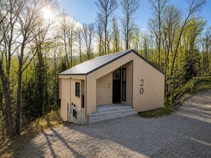 A small, single-story wooden cabin with a sloped roof, a door, and a number '20' on the side, surrounded by trees and a gravel path. - Spa & Foosball | Le WKD (Saint-Philémon)