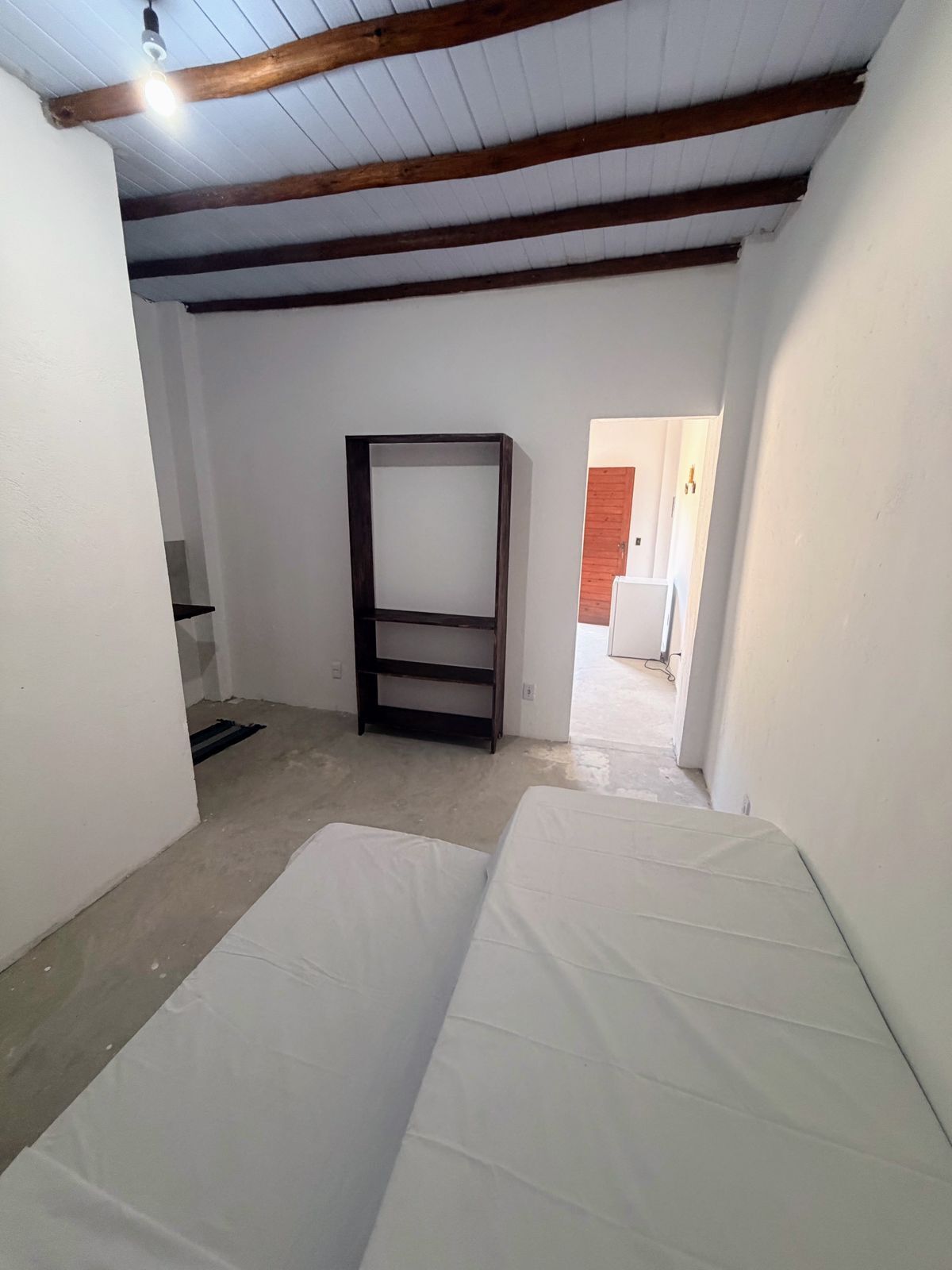 A room with white walls, a wooden ceiling, and a metal-framed shelf.