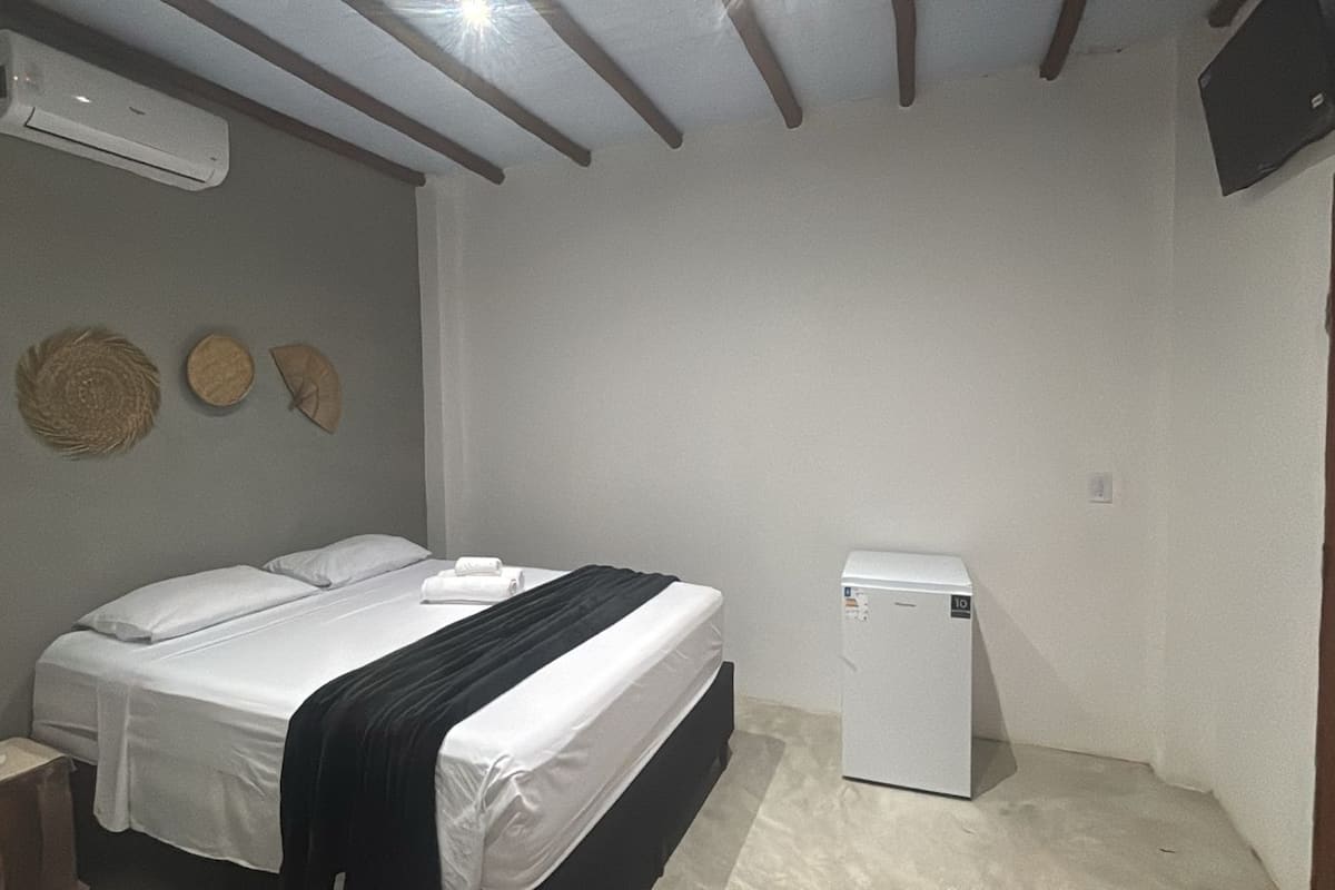 A bedroom with a bed, a small white refrigerator, and a wall-mounted air conditioner.