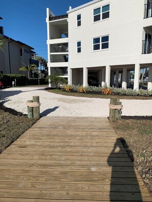 A wooden pathway leading to a white building with multiple balconies and a gated entrance. - IT'S A SHORE THING - 
ON THE BEACH - SPECTACULAR SUNSETS
NEWLY RENOVATED (Fort Myers Beach)
