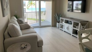 A living room with a beige sofa, a small round table, a white cabinet, and a TV mounted on the wall. - IT'S A SHORE THING - 
ON THE BEACH - SPECTACULAR SUNSETS
NEWLY RENOVATED (Fort Myers Beach)