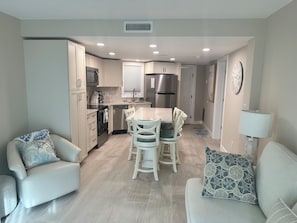 A modern kitchen with white cabinets, a stainless steel refrigerator, and a dining area with a white table and chairs. - IT'S A SHORE THING - 
ON THE BEACH - SPECTACULAR SUNSETS
NEWLY RENOVATED (Fort Myers Beach)