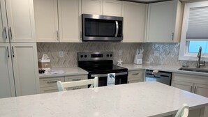 A modern kitchen with white cabinets, a black microwave, stainless steel appliances, and a marble countertop. - IT'S A SHORE THING - 
ON THE BEACH - SPECTACULAR SUNSETS
NEWLY RENOVATED (Fort Myers Beach)